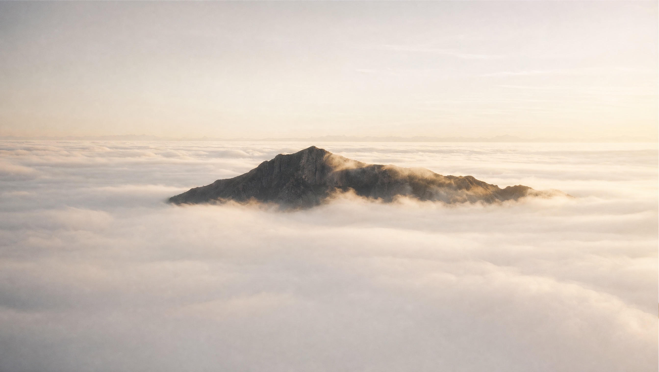 A mountain ridge emerges into sunlight above a sea of morning fog that hides the landscape below.